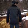 Person wearing a black jacket and cowboy hat standing in a snowy landscape with hay bales.