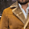 Brown suede jacket with fur collar worn by a person, blurred background