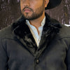 Man wearing a dark coat with a fur collar against a blurred natural background