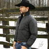 Man wearing a black puffer jacket and cowboy hat standing in front of a wooden fence with snow on the ground.