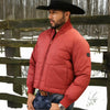 Man wearing a red puffer jacket and black cowboy hat standing in front of a wooden fence with snow on the ground.