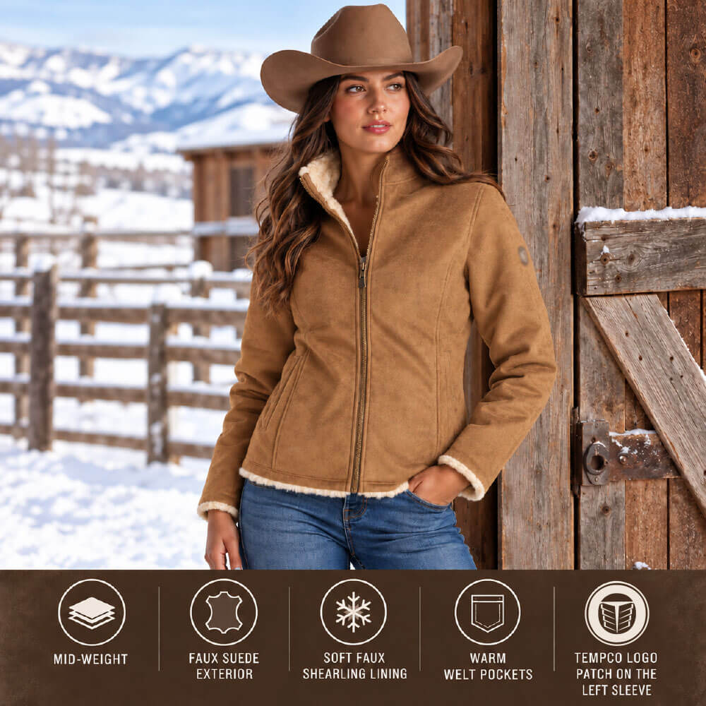 A woman wearing a brown shearling-lined jacket, blue jeans, and a brown cowboy hat stands outdoors in front of a wooden barn door with a snowy mountain landscape in the background. A dark brown informational banner at the bottom lists product features: mid-weight, faux suede exterior, soft faux shearling lining, warm welt pockets, and a tempco logo patch on the left sleeve.