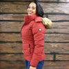 Woman wearing a red puffer jacket with fur-lined hood against a wooden wall.