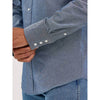 Close-up of a person wearing a blue denim shirt with rolled-up sleeves on a white background