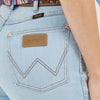 Close-up of a person wearing light blue jeans with a brown leather label on the back pocket, featuring the 'Wrangler' brand.